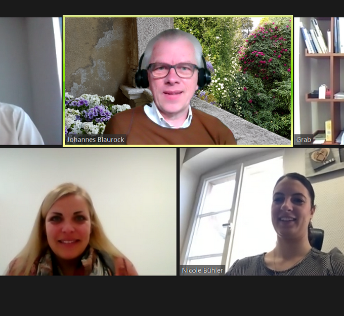 Ein Screenshot eines virtuellen Meetings mit drei Personen zeigt ein vielfältiges Team, das an einem Projekt zusammenarbeitet. Der obere Mann in der Mitte, mit Kopfhörern und einem Naturhintergrund, wird von zwei Frauen flankiert: eine mit blondem Haar auf der linken Seite und die andere mit dunkelbraunem Haar auf der rechten Seite. Hinter ihnen ist teilweise ein Bücherregal sichtbar.