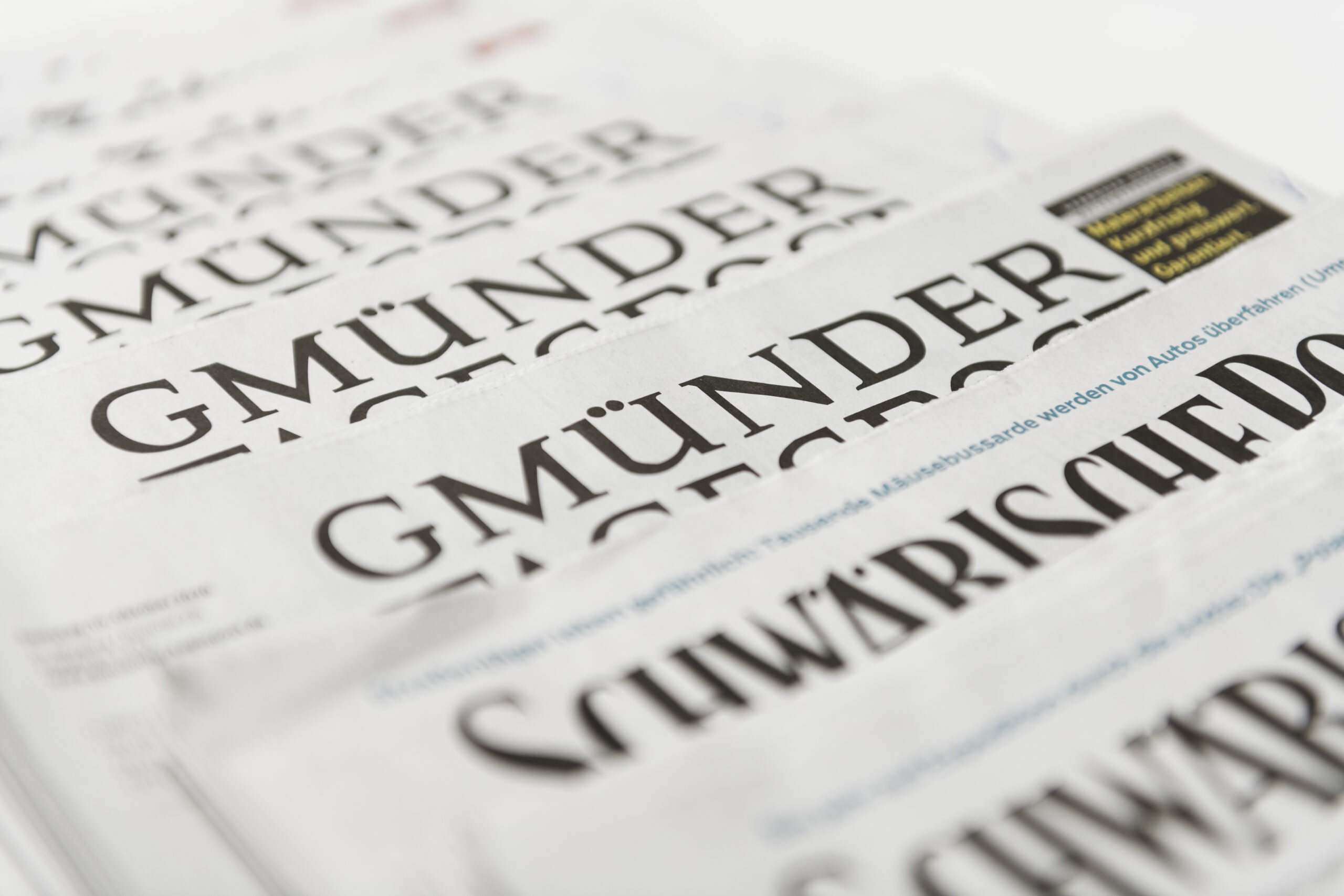 Auf einer hellen Unterlage liegt ein Stapel Zeitungen mit Schlagzeilen der „Gmünder Tagespost“ und der „Schwäbischen“. Unter anderem geht es um das Thema Pflege und die Bedeutung des Corona-Bonus.