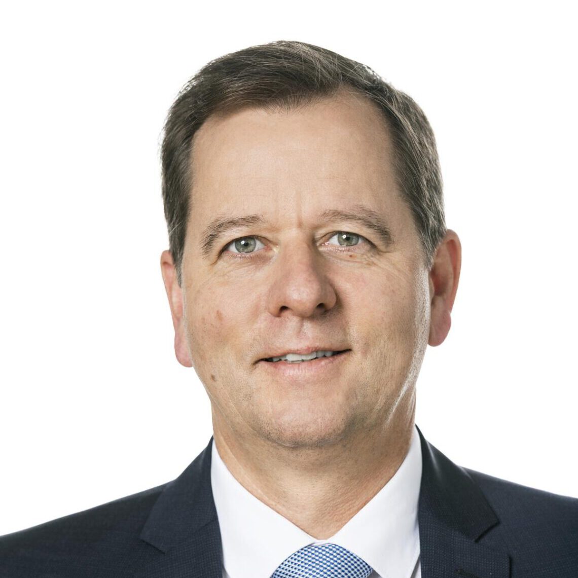 Eine Person mit kurzen dunklen Haaren, einem blauen Anzug, einem weißen Hemd und einer hellblauen Krawatte steht vor einem weißen Hintergrund. Dieses Vorstandsmitglied blickt mit neutralem Gesichtsausdruck nach vorne und verkörpert damit ein Ethos der Teilhabe und des Engagements für Inklusion.
.