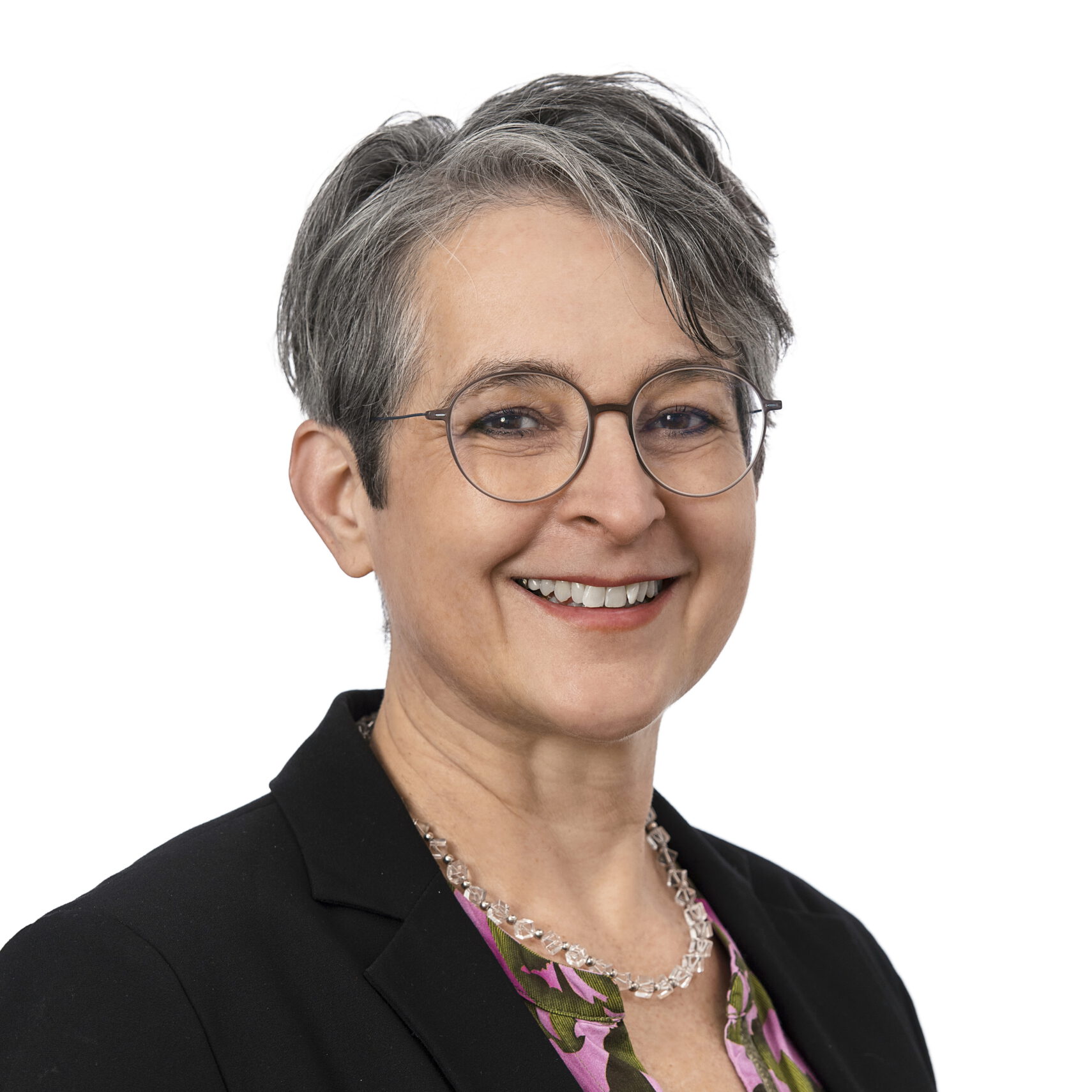 Eine lächelnde Person mit kurzen grauen Haaren und Brille, die einen schwarzen Blazer, ein lila gemustertes Oberteil und eine durchsichtige Perlenkette trägt, posiert vor einem weißen Hintergrund im Quartiersprojekt Waldstetten. Eine lächelnde Person mit kurzen grauen Haaren und Brille, die einen schwarzen Blazer, ein lila gemustertes Oberteil und eine durchsichtige Perlenkette trägt, posiert vor einem weißen Hintergrund im Quartiersprojekt Waldstetten.