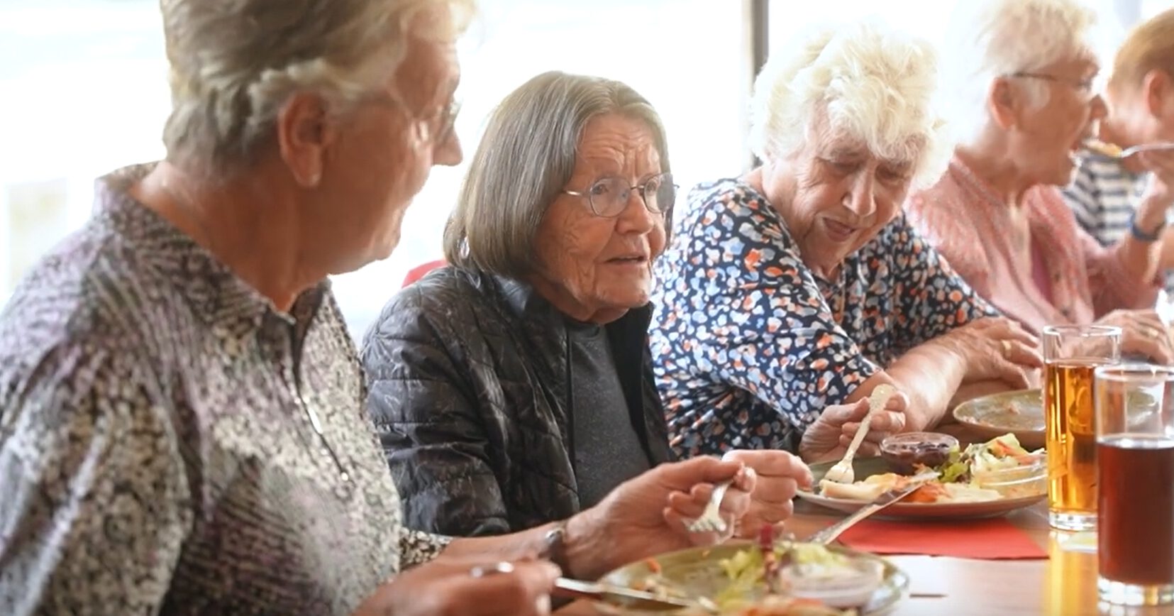 Drei ältere Damen sitzen bei einem gemütlichen Beuremer Mittagstisch zusammen an einem Tisch, genießen ihr Mittagessen und unterhalten sich angeregt, ihre Teller sind mit köstlichen Speisen und Getränken gefüllt.