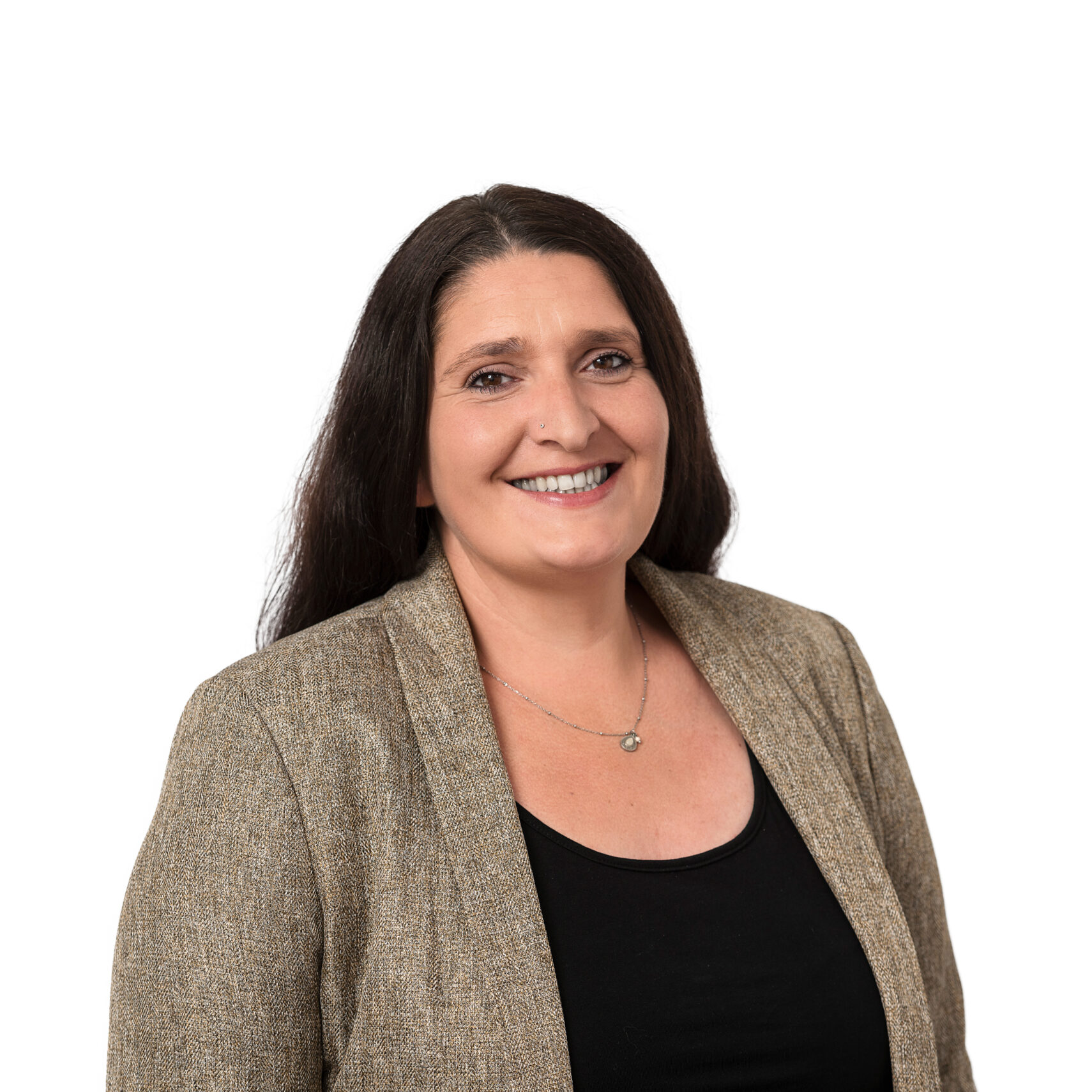 Eine Frau mit langen dunklen Haaren, die einen hellbraunen Blazer über einem schwarzen Oberteil trägt, lächelt vor einem schlichten weißen Hintergrund in die Kamera und verkörpert Professionalität und Selbstvertrauen, die für ein effektives Anfragemanagement unerlässlich sind.