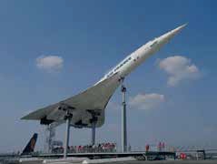 Ein Überschall-Passagierflugzeug vom Typ Concorde steht im Technikmuseum Sinsheim auf schrägen Stützpfeilern im Freien, darunter eine Gruppe von Menschen und im Hintergrund ein blauer Himmel mit Wolken.