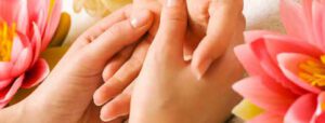 Zwei Hände geben sanft eine Handmassage, umgeben von rosa Lotusblumen, die eine ruhige und beruhigende Spa-Atmosphäre schaffen.