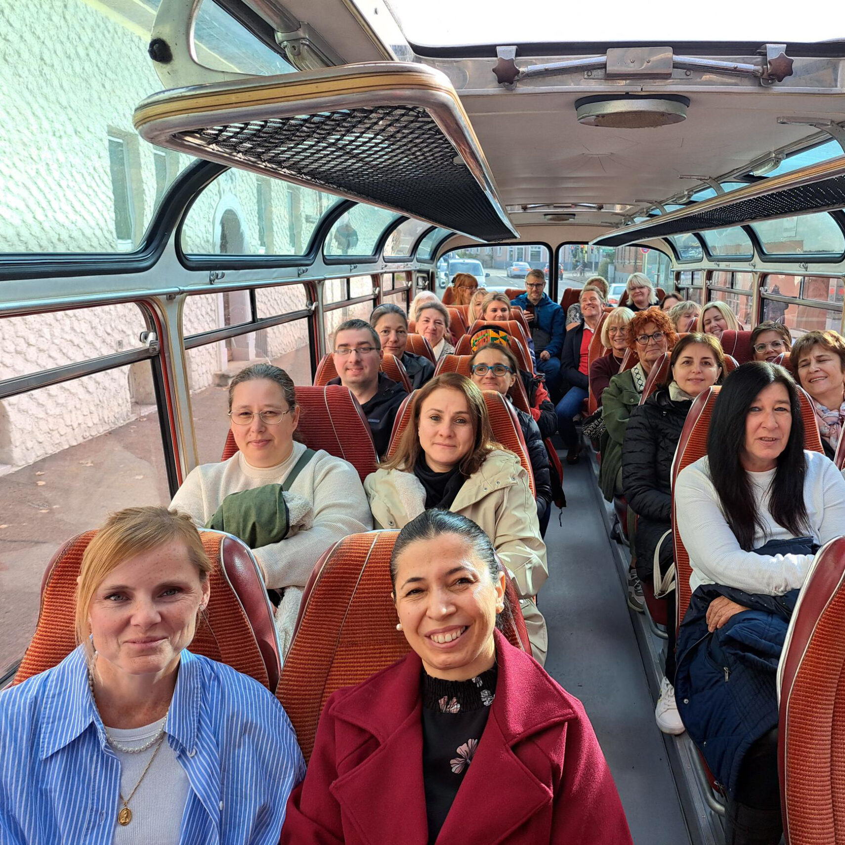 Eine Gruppe von Menschen sitzt in einem Bus mit großen Fenstern und roten Sitzen, lächelt und schaut in die Kamera. Die fröhliche, bunt gemischte Gruppe scheint bereit für einen Ausflug, möglicherweise im Rahmen eines Altenhilfe-Ausflugs oder einer Jubilarfeier. Eine Gruppe von Menschen sitzt in einem Bus mit großen Fenstern und roten Sitzen, lächelt und schaut in die Kamera. Die fröhliche, bunt gemischte Gruppe scheint bereit für einen Ausflug, möglicherweise im Rahmen eines Altenhilfe-Ausflugs oder einer Jubilarfeier.