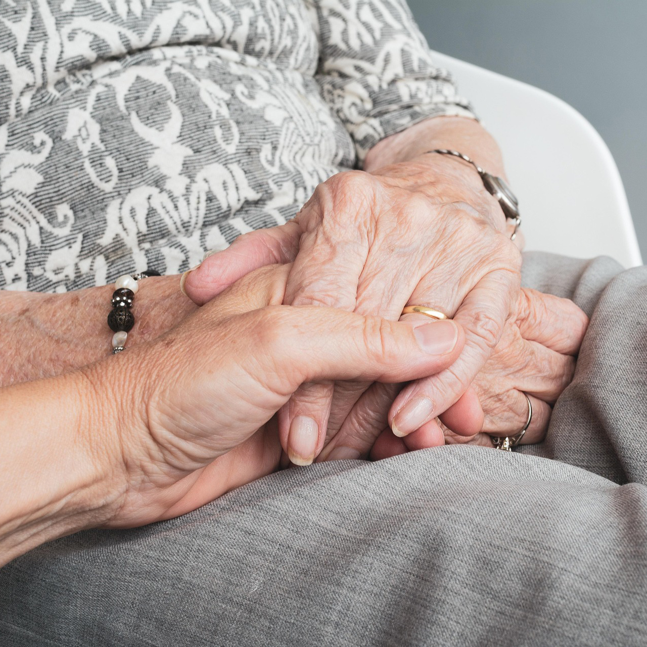 Eine Nahaufnahme von zwei Menschen, die sich an den Händen halten, zeigt die Hände einer älteren Person, die auf ihrem Schoß ruht, und eine jüngere Hand, die sie sanft umschließt und Trost und Unterstützung vermittelt – ein automatisch gespeicherter Entwurf von Mitgefühl über Generationen hinweg. Eine Nahaufnahme von zwei Menschen, die sich an den Händen halten, zeigt die Hände einer älteren Person, die auf ihrem Schoß ruht, und eine jüngere Hand, die sie sanft umschließt und Trost und Unterstützung vermittelt - ein automatisch gespeicherter Entwurf von Mitgefühl über Generationen hinweg.